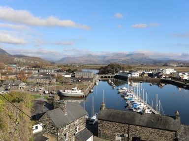 A harbor with boats docked near stone buildings and mountains in the background at Wynding Apartment in Amble-By-The-Sea