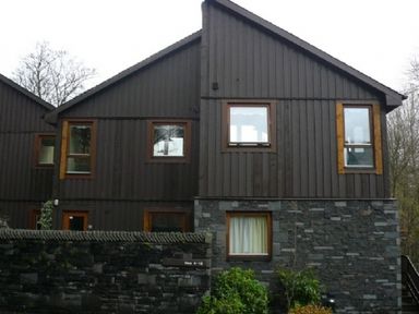 A house with dark wooden upper walls and stone lower walls with several windows and a small garden in front at 13 Keswick Bridge in Keswick