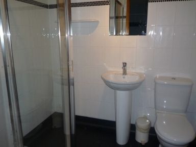 A bathroom with a shower, pedestal sink, toilet, small trash bin, and mirror at 13 Keswick Bridge in Keswick