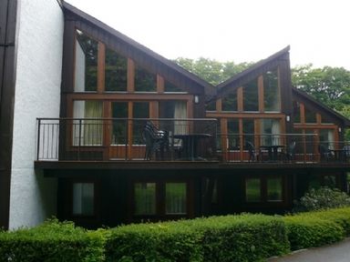 An exterior view of a building with large triangular windows and balconies with tables and chairs at 13 Keswick Bridge in Keswick