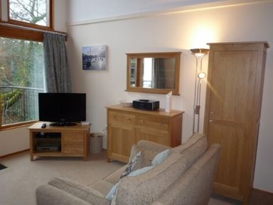 A living room with a television, wooden cabinets, a sofa, and a floor lamp at 10 Keswick Bridge in Keswick