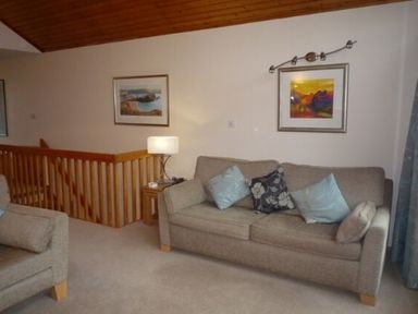 A living room with a sofa and armchair cushions a lamp and framed paintings on the walls at 10 Keswick Bridge in Keswick