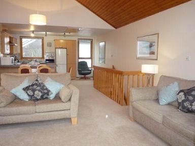 A living room with two sofas and cushions next to a kitchen and wooden staircase at 10 Keswick Bridge in Keswick