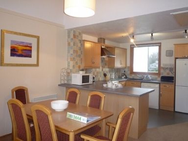 A kitchen and dining area with a table and chairs a microwave and a refrigerator at 10 Keswick Bridge in Keswick