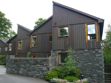 A row of modern houses with wood paneling and stone walls with some greenery at 16 Keswick Bridge in Keswick