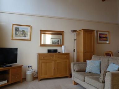 A living room with a beige sofa and blue cushions wooden cabinets and a television at 16 Keswick Bridge in Keswick