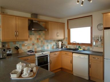 A kitchen with wooden cabinets white dishwasher and window at 16 Keswick Bridge in Keswick