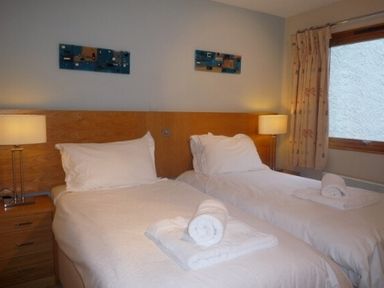 A bedroom with two single beds with white bedding and rolled towels bedside lamps and a window at 16 Keswick Bridge in Keswick
