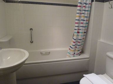A bathroom with a bathtub sink toilet and a striped shower curtain at 16 Keswick Bridge in Keswick