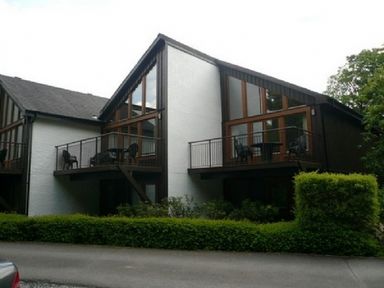 A two-story building with balconies and outdoor chairs surrounded by greenery at 6 Keswick Bridge in Keswick