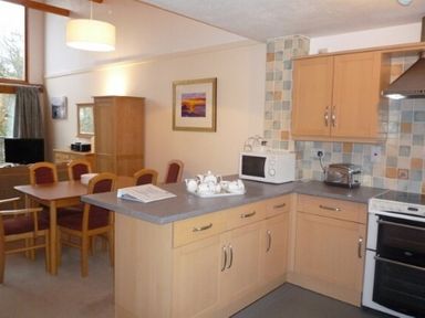 A kitchen and dining area with wooden cabinets a dining table with chairs and appliances at 6 Keswick Bridge in Keswick
