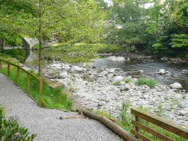 A gravel path with wooden railing next to a rocky river with trees in Keswick