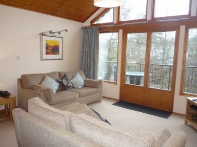A living room with two beige sofas and large wooden framed windows at 19 Keswick Bridge in Keswick