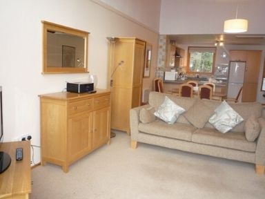 A living room with a beige sofa and wooden furniture including a sideboard wardrobe and dining table at 20 Keswick Bridge in Keswick