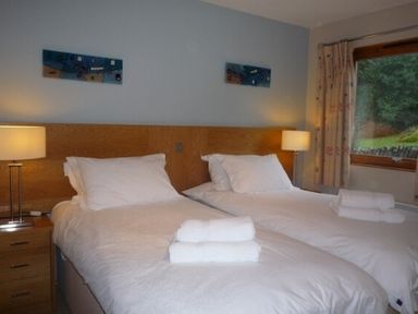 A bedroom with two single beds each with white linens and towels bedside tables with lamps and a window at 20 Keswick Bridge in Keswick