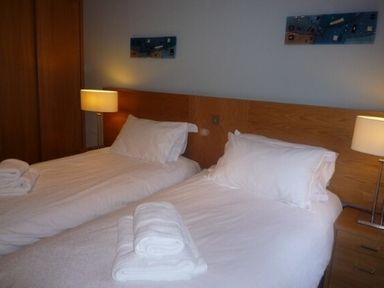 A bedroom with two single beds with white linens and towels on them with lamps and wooden headboard at 20 Keswick Bridge in Keswick