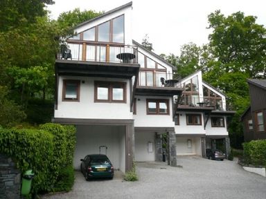 Three modern white houses with balconies and cars parked under them surrounded by trees and greenery at 21 Keswick Bridge in Keswick