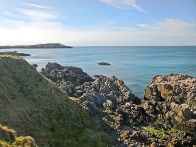Rocky coastline with grassy cliffs and calm sea at Angorfa in Cemaes Bay