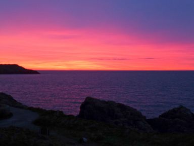 A sunset over the ocean with rocky cliffs in the foreground at Angorfa in Cemaes Bay