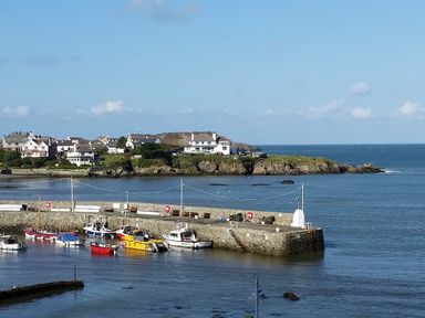 A small harbor with boats docked and houses on a rocky shoreline in the background at Angorfa in Cemaes Bay