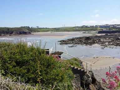 A coastal scene with a sandy beach rocks a stairway with a handrail and houses on the hillside at Angorfa in Cemaes Bay