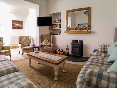 A living room with armchairs and sofas around a wooden coffee table near a wood stove with a mirror above at Angorfa in Cemaes Bay