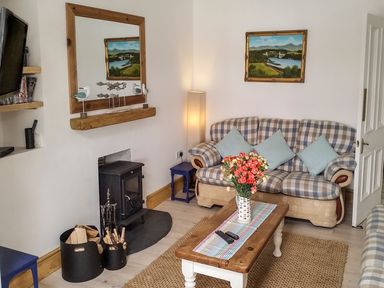 A living room with a checked sofa blue cushions a wooden coffee table with flowers a fireplace and a large mirror at Angorfa in Cemaes Bay