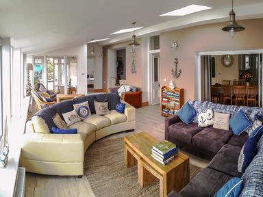 A living room with two sofas a wooden coffee table a small bookshelf and dining area at Angorfa in Cemaes Bay