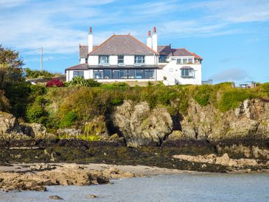 A large house on a cliff overlooking a rocky beach and water at Angorfa in Cemaes Bay
