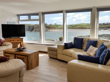 A living room with beige leather sofas blue cushions wooden coffee table near large windows showing a coastal view at Angorfa in Cemaes Bay