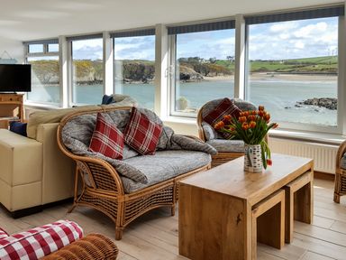 A living room with wicker chairs and a wooden coffee table overlooking a coastal view at Angorfa in Cemaes Bay
