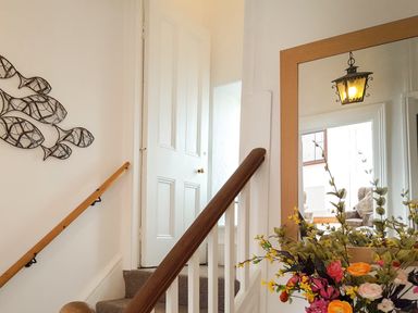 A staircase with wooden handrails a wall decoration of fish a mirror reflecting a light and chairs with flowers in front at Angorfa in Cemaes Bay