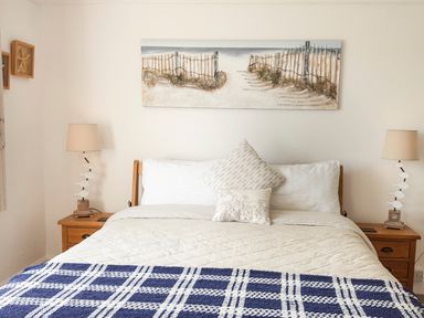 A bedroom with a bed with white bedding and pillows two wooden bedside tables with lamps and a painting above the bed at Angorfa in Cemaes Bay