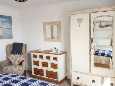 A bedroom with a wooden dresser a mirror a wardrobe an armchair and a bed with a blue checkered blanket at Angorfa in Cemaes Bay
