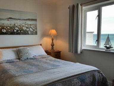 A bedroom with a bed a nightstand lamp a window with curtains and a model sailboat at Angorfa in Cemaes Bay