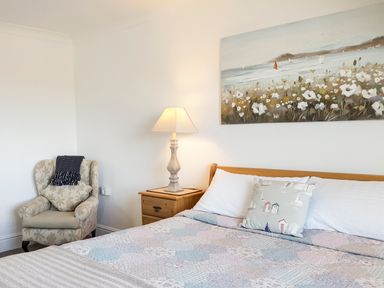 A bedroom with a bed pillow armchair wooden nightstand table lamp and landscape painting at Angorfa in Cemaes Bay