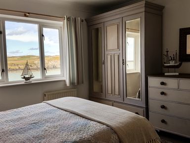 A bedroom with a bed next to a window wardrobe with mirrors and a chest of drawers with model boats on top at Angorfa in Cemaes Bay