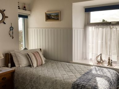 A bedroom with a single bed a bedside table with lamp and decorative items on the window at Angorfa in Cemaes Bay