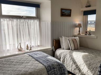 A bedroom with two single beds a lamp and decorative items on window sills at Angorfa in Cemaes Bay