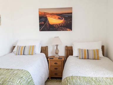 A bedroom with two single beds a nightstand and a painting of a boat at Angorfa in Cemaes Bay