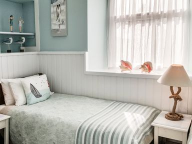 A bedroom with a bed a bedside table a lamp and decorative items on shelves and a windowsill at Angorfa in Cemaes Bay