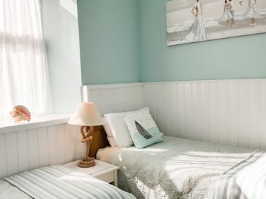 A bedroom with two single beds a nightstand with a lamp a window with sheer curtains and a painting on the wall at Angorfa Cemaes Bay