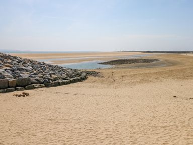 A sandy beach with a rock barrier on the left and water pools at Castle School House in Kidwelly