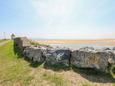A coastal path with a stone wall and a lighthouse near a sandy beach at Castle School House in Kidwelly