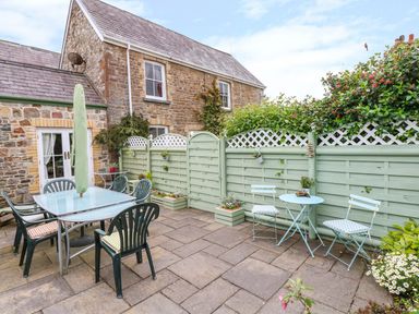 An outdoor patio with tables chairs an umbrella and a green wooden fence at Castle School House in Kidwelly