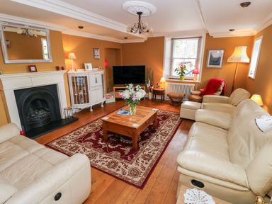 A living room with beige sofas a wooden coffee table with flowers a large rug a fireplace and a television at Castle School House in Kidwelly