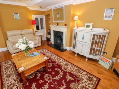 A living room with a beige sofa wooden coffee table flowers fireplace and white cabinet at Castle School House in Kidwelly