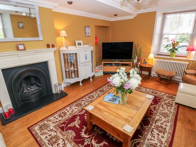A living room with a wooden coffee table with flowers and books on a red patterned rug and a television at Castle School House in Kidwelly
