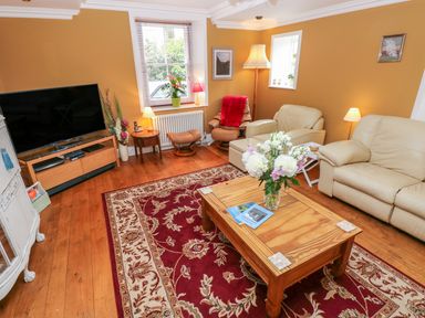 A living room with beige leather sofas a wooden coffee table with flowers and a red patterned rug at Castle School House in Kidwelly