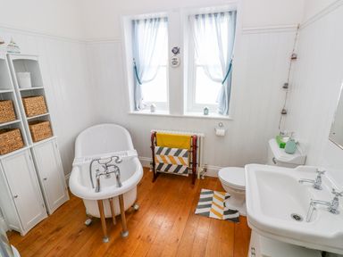 A bathroom with a clawfoot bathtub a sink toilet shelving unit and two windows at Castle School House in Kidwelly